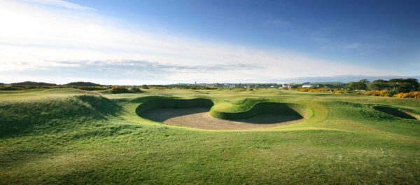 Deep bunkers and lush green grass set against a clear blue sky at the Old Course, St Andrews
