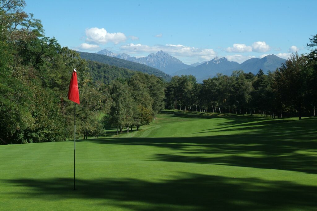 A red flag, tree lined fairway and alpine backdrop at Circolo Golf Villa Deste