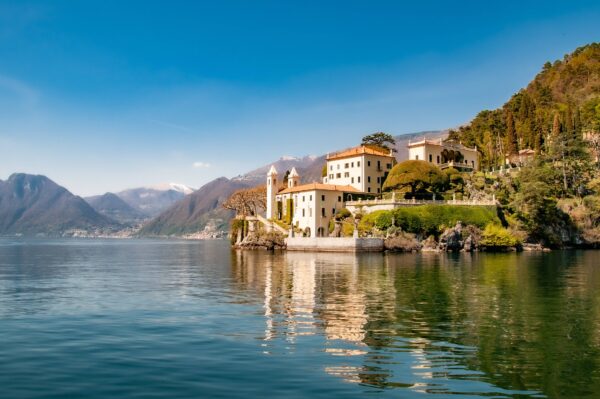 Large whitewash villa with terracotta tiled roof on the side of Lake Como, Italy. With background views of the snow capped Alps